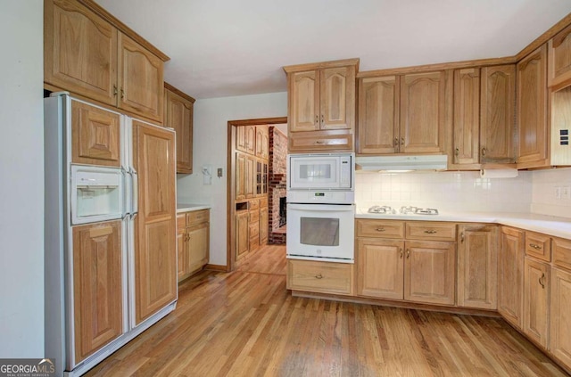 kitchen featuring light wood finished floors, decorative backsplash, built in appliances, light countertops, and under cabinet range hood