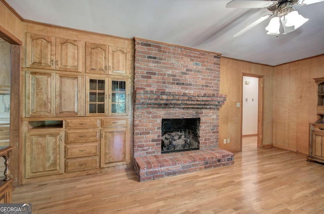 living area with light wood finished floors, wooden walls, ceiling fan, ornamental molding, and a brick fireplace