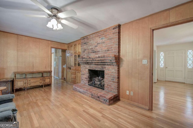 unfurnished living room with light wood-type flooring, a brick fireplace, ceiling fan, and wooden walls