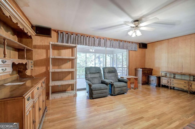 sitting room featuring wooden walls, light wood-style flooring, and a ceiling fan