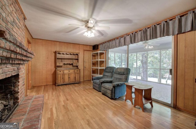 sitting room with wood walls, ceiling fan, a fireplace, and wood finished floors