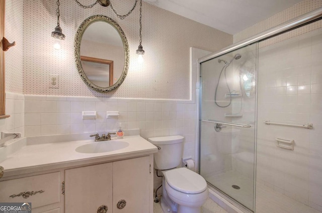 bathroom with a wainscoted wall, toilet, a stall shower, vanity, and wallpapered walls