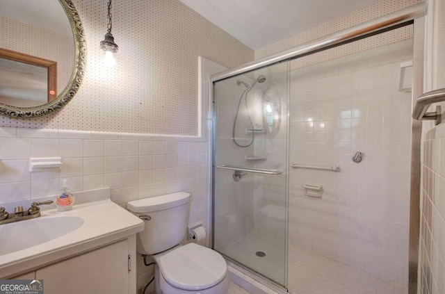 bathroom with toilet, tile walls, wainscoting, a stall shower, and wallpapered walls