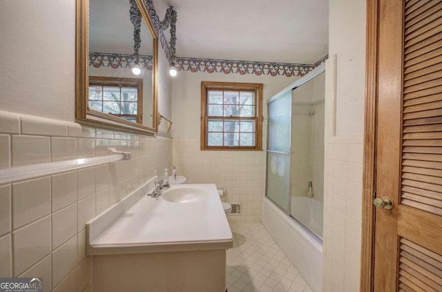 bathroom with plenty of natural light, combined bath / shower with glass door, tile walls, and vanity