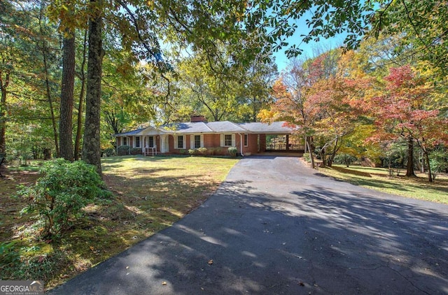 single story home with a chimney, aphalt driveway, an attached carport, and a front yard