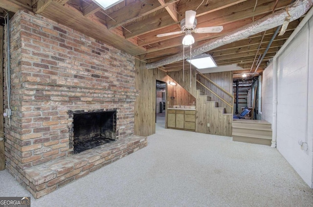 unfurnished living room with carpet, stairway, a ceiling fan, a brick fireplace, and wood walls