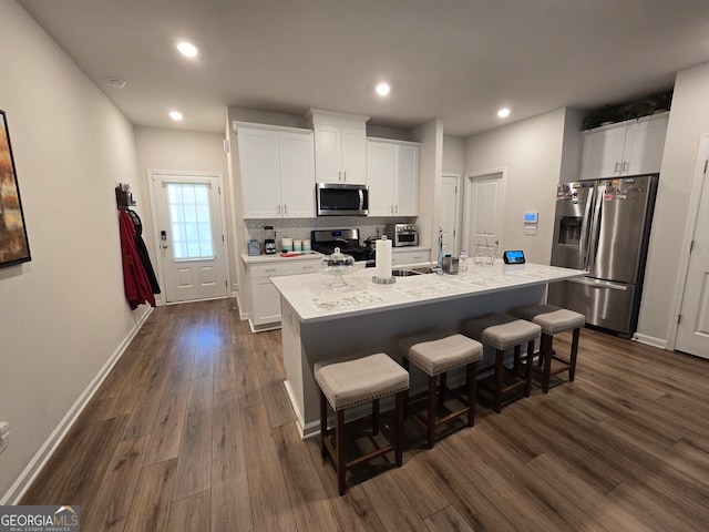 kitchen featuring a kitchen bar, white cabinetry, a kitchen island with sink, and appliances with stainless steel finishes