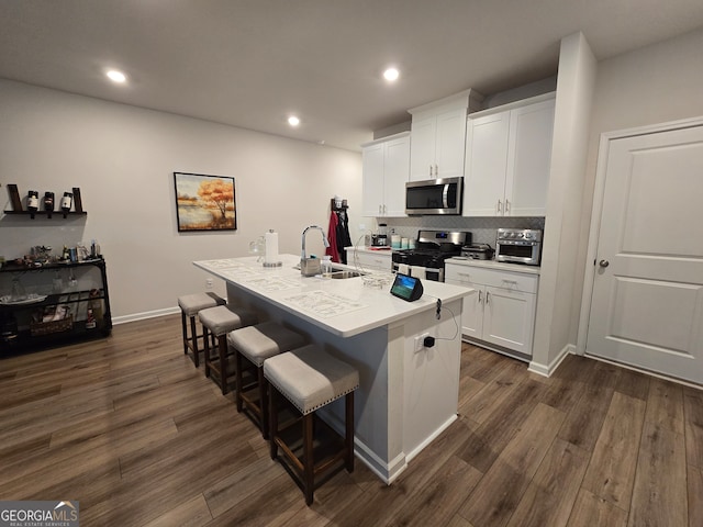 kitchen with dark wood-type flooring, white cabinetry, a kitchen island with sink, and appliances with stainless steel finishes