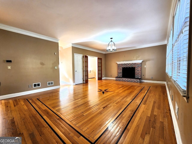 unfurnished living room with wood-type flooring, a notable chandelier, ornamental molding, and a brick fireplace