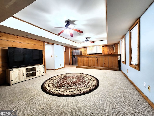 unfurnished living room featuring wood walls, a tray ceiling, light carpet, and ceiling fan