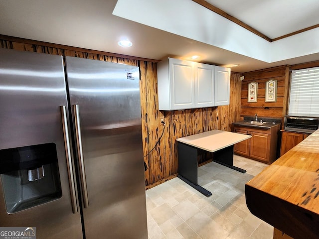 kitchen featuring wood walls, white cabinetry, sink, stainless steel refrigerator with ice dispenser, and butcher block countertops