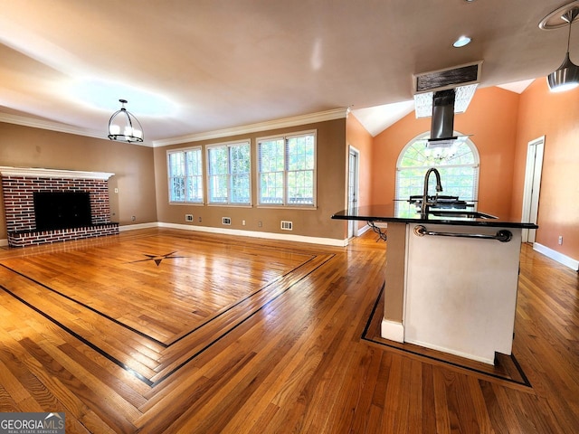 kitchen featuring crown molding, decorative light fixtures, sink, hardwood / wood-style flooring, and an island with sink