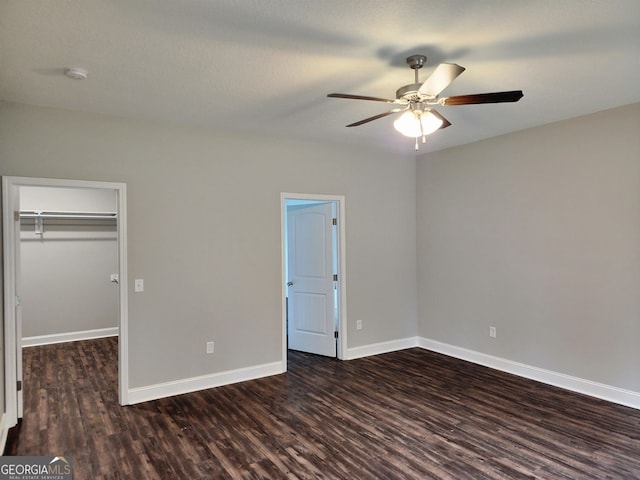 unfurnished bedroom with dark wood-type flooring, ceiling fan, a closet, and a spacious closet