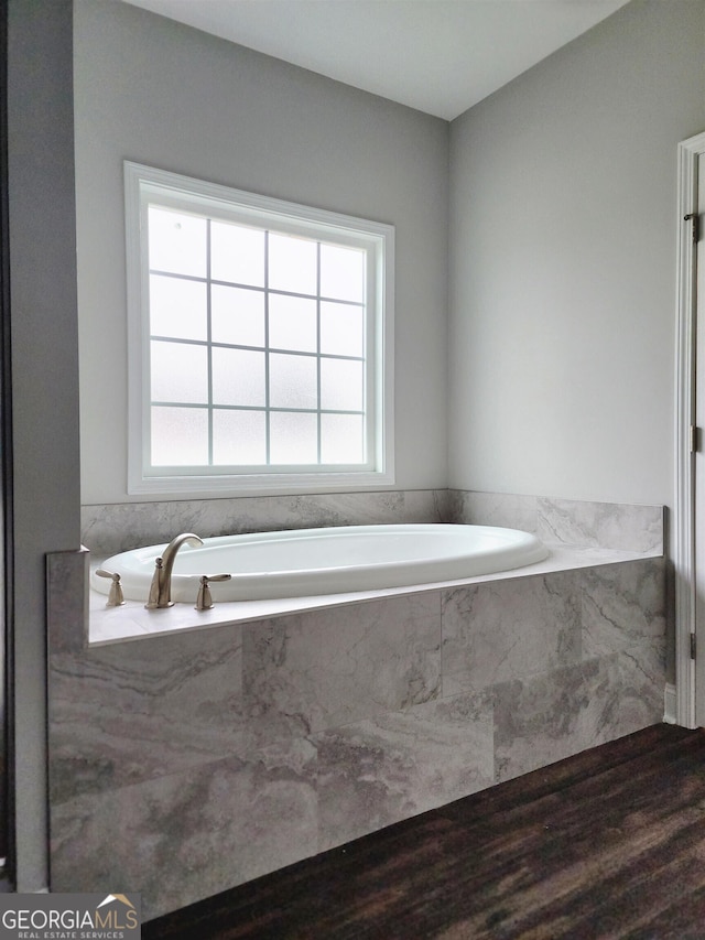 bathroom with a relaxing tiled tub and hardwood / wood-style floors