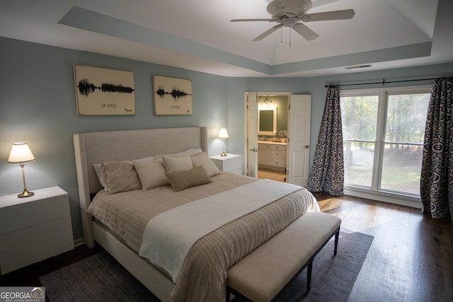 bedroom with ceiling fan, a raised ceiling, wood-type flooring, and connected bathroom