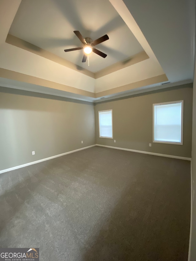 carpeted spare room featuring ceiling fan and a raised ceiling