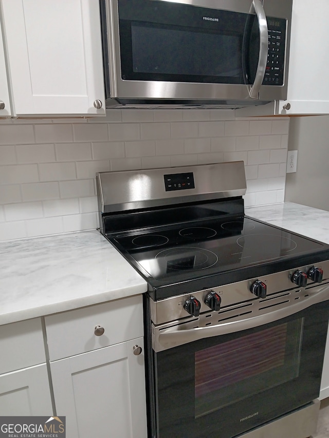 kitchen featuring white cabinetry, light stone countertops, stainless steel appliances, and backsplash