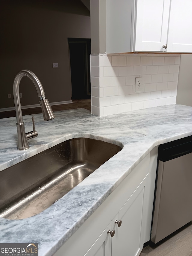 kitchen with stainless steel dishwasher, sink, white cabinets, and light stone counters