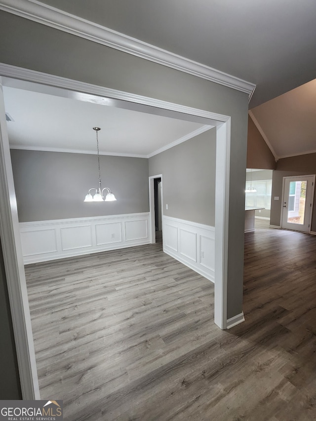 unfurnished dining area with hardwood / wood-style floors, lofted ceiling, a chandelier, and crown molding