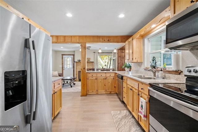 kitchen with light brown cabinets, stainless steel appliances, sink, pendant lighting, and light hardwood / wood-style floors