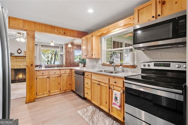 kitchen with sink, a brick fireplace, light wood-type flooring, appliances with stainless steel finishes, and ceiling fan