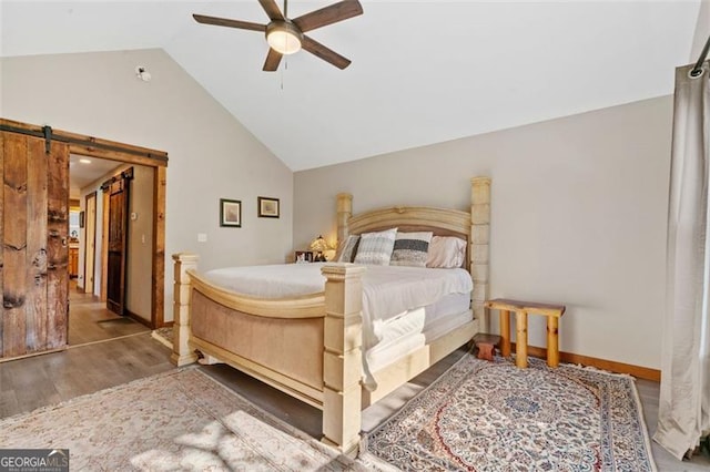 bedroom with a barn door, hardwood / wood-style flooring, vaulted ceiling, and ceiling fan