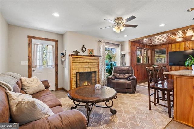 living room featuring wooden walls, a fireplace, and ceiling fan