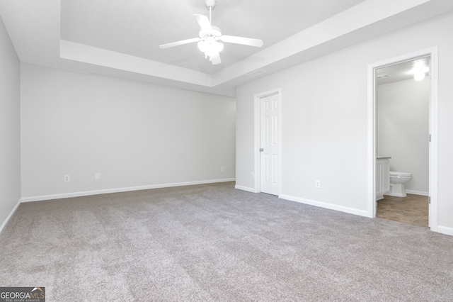 unfurnished bedroom featuring ensuite bath, carpet flooring, a tray ceiling, and ceiling fan