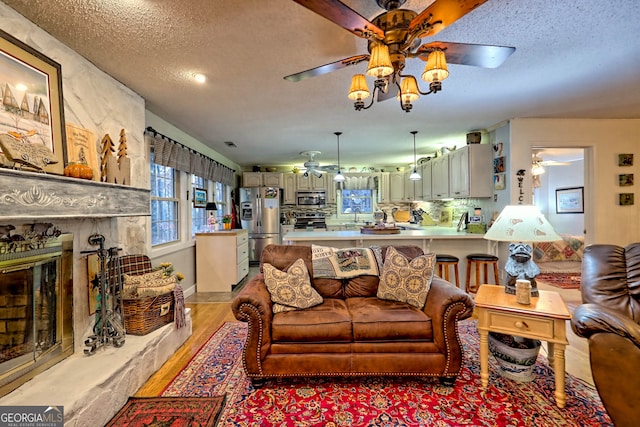 living room featuring a fireplace, a textured ceiling, light wood-type flooring, and ceiling fan