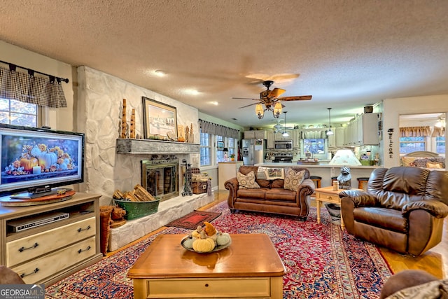 living room featuring a stone fireplace, ceiling fan, hardwood / wood-style floors, and a textured ceiling