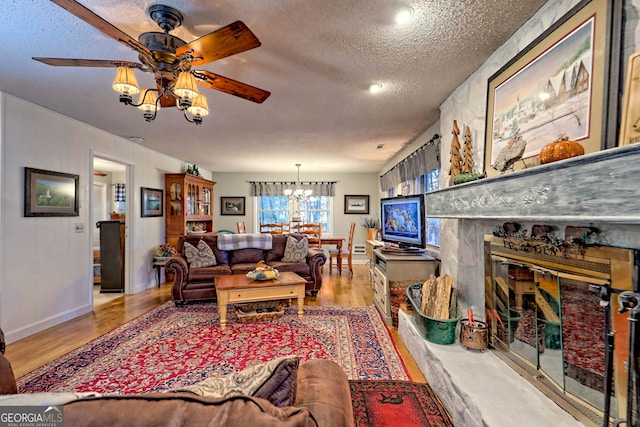 living room with a fireplace, a textured ceiling, light hardwood / wood-style floors, and ceiling fan with notable chandelier