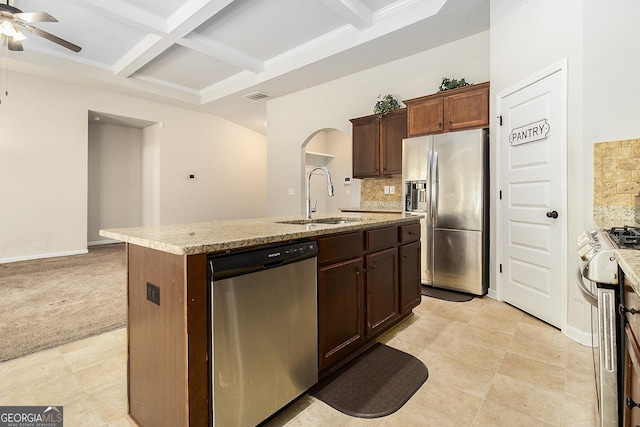 kitchen featuring coffered ceiling, stainless steel appliances, sink, beam ceiling, and an island with sink