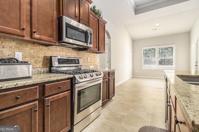 kitchen with decorative backsplash, stainless steel appliances, light stone counters, and crown molding