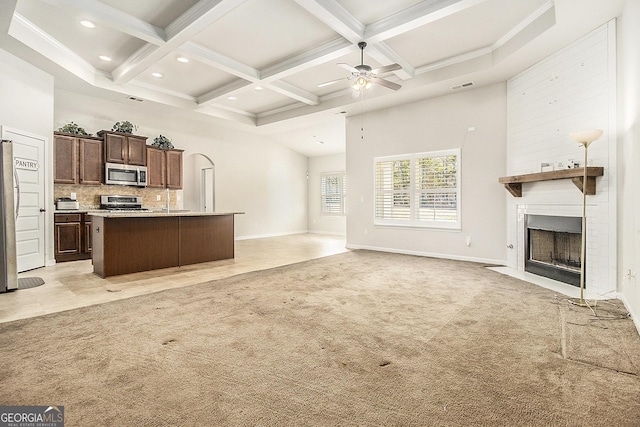 unfurnished living room with light carpet, a towering ceiling, coffered ceiling, a large fireplace, and ceiling fan