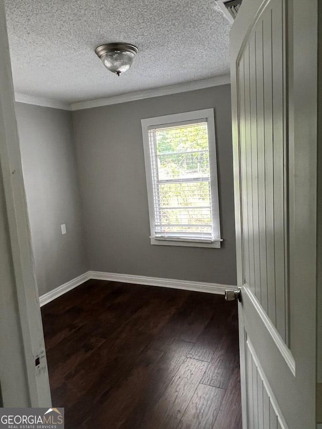 spare room featuring dark wood-type flooring, a textured ceiling, and ornamental molding