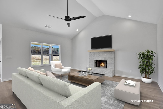 living room with hardwood / wood-style flooring, ceiling fan, a fireplace, and vaulted ceiling