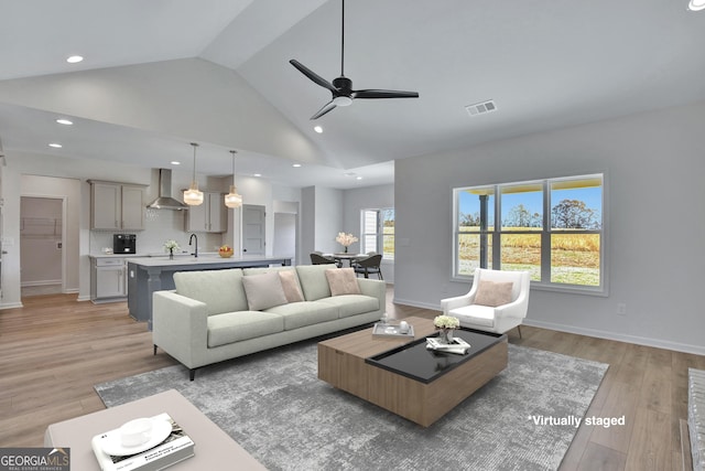 living room with ceiling fan, light wood-type flooring, sink, and high vaulted ceiling