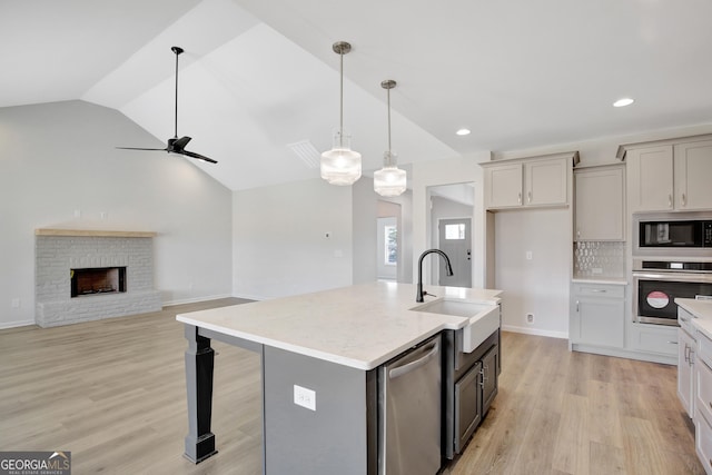 kitchen with light wood-type flooring, stainless steel appliances, vaulted ceiling, a kitchen island with sink, and sink