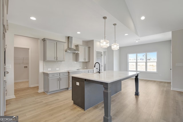 kitchen featuring gray cabinetry, a breakfast bar, lofted ceiling, wall chimney range hood, and hanging light fixtures