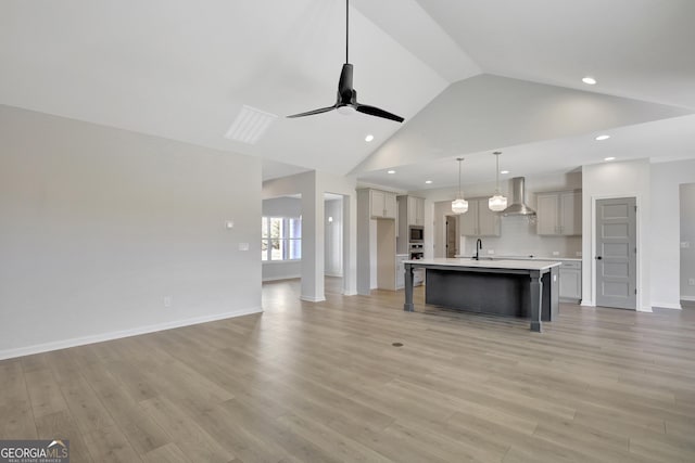 kitchen with ceiling fan, sink, wall chimney range hood, a center island with sink, and light hardwood / wood-style floors