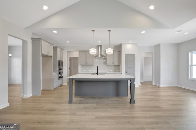 kitchen featuring lofted ceiling, wall chimney range hood, sink, an island with sink, and appliances with stainless steel finishes