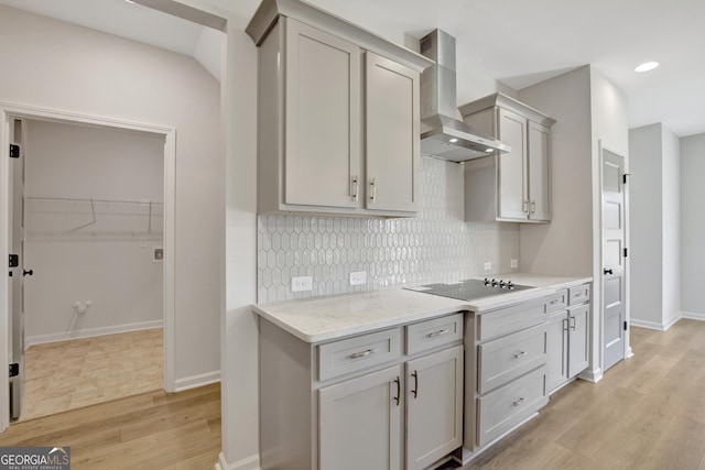 kitchen with tasteful backsplash, black electric cooktop, wall chimney range hood, light hardwood / wood-style flooring, and gray cabinets