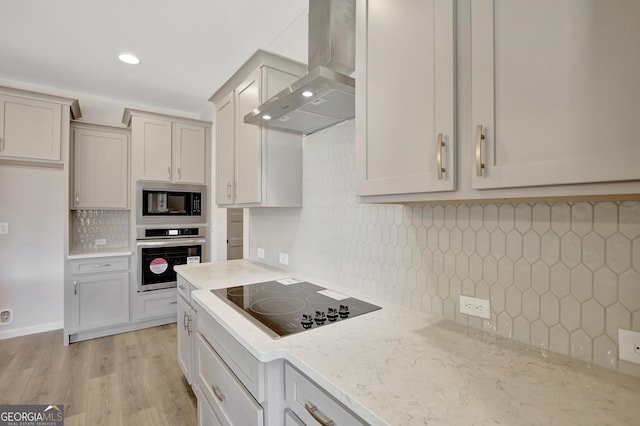 kitchen featuring backsplash, black appliances, light hardwood / wood-style flooring, wall chimney exhaust hood, and light stone countertops