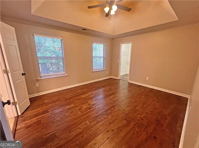 empty room featuring dark hardwood / wood-style flooring, ceiling fan, and a raised ceiling