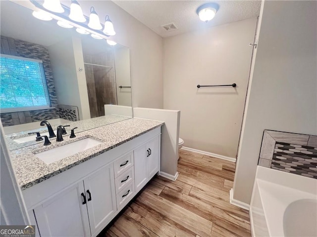 bathroom with a textured ceiling, a tile shower, hardwood / wood-style floors, vanity, and toilet