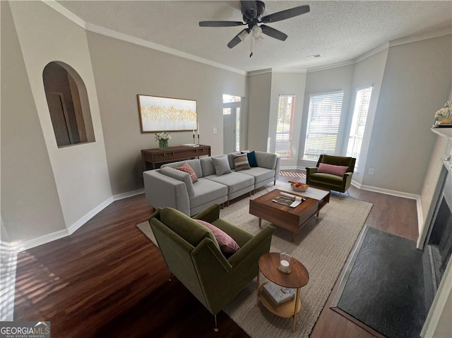 living room with a textured ceiling, ornamental molding, dark hardwood / wood-style floors, ceiling fan, and a fireplace