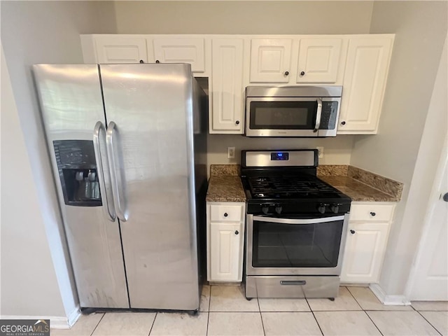 kitchen with dark stone counters, white cabinetry, light tile patterned floors, and stainless steel appliances