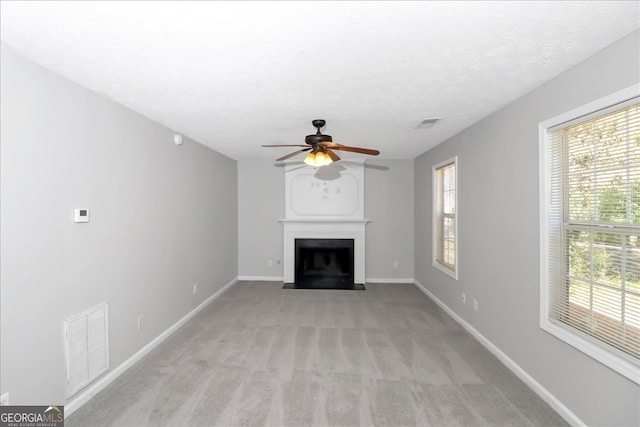 unfurnished living room with ceiling fan, light carpet, a textured ceiling, and plenty of natural light