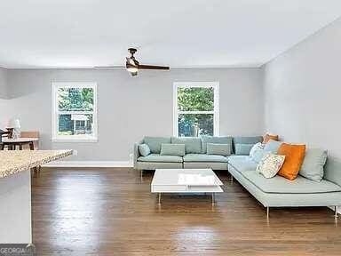 living room featuring dark wood-type flooring, ceiling fan, and plenty of natural light