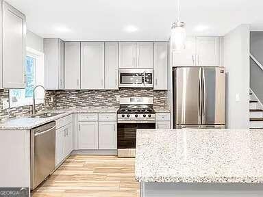 kitchen featuring hanging light fixtures, stainless steel appliances, sink, light stone countertops, and light hardwood / wood-style floors